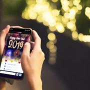Woman Hand holding mobile see live streaming countdown to Happy new year 2019 with fireworks over cityscape on screen with light bokeh background,Digital social media lifestyle